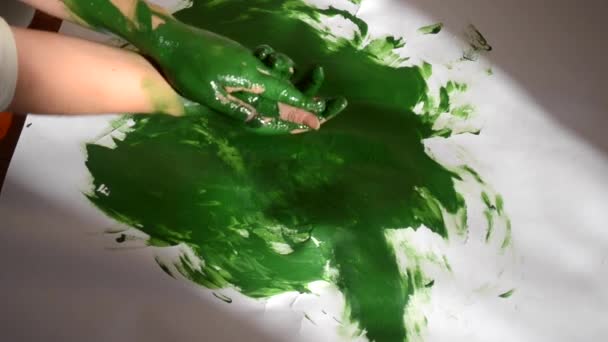 Meisje smeert groene verf op de handen en tekent op papier — Stockvideo