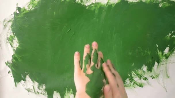 Chica unta pintura verde en las manos y dibuja en papel — Vídeos de Stock