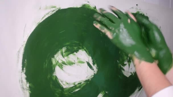 Girl smears green paint on the hands and draws on paper — Stock Video