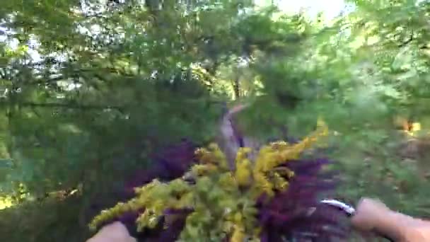 女孩骑着自行车走在森林小径上，手里拿着一束花 — 图库视频影像