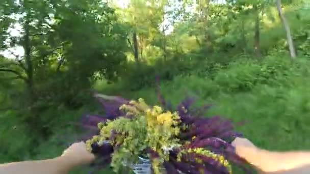 Fille monte un vélo avec un bouquet de fleurs devant la roue — Video