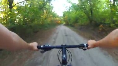 Gün batımında geniş toprak bir yolda bisiklet süren bir insan.