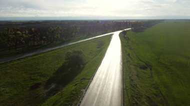 İnsansız hava aracı ıslak asfalt yolda ekili tarlalar arasındaki arabalar için iniyor.