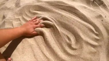 İnsan elini kumdan yüzeye uzatır ve parmaklarıyla dağıtır.