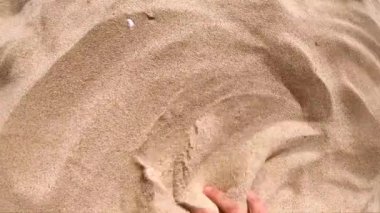 İnsan elini kumdan yüzeye uzatır ve parmaklarıyla dağıtır.