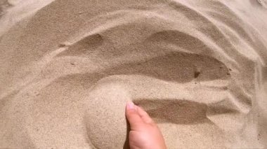 Avucundaki bir avuç kumu kepçeleyen kız parmaklarının arasından kumu saçıyor.