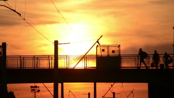 Mensen lopen gaan de brug tegen de achtergrond ondergaande zon — Stockvideo