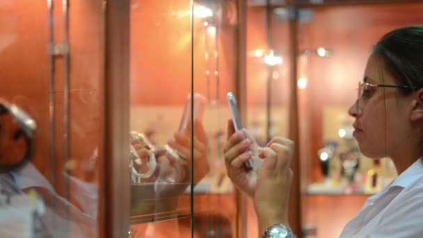 Girl photographs phone wristwatch in a shop window — Stock Video