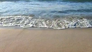 Güneşli bir yaz gününde kumlu bir kumsalda mavi şeffaf suyla dalgalar yuvarlanıyor. Doğa arkaplanı. Doğal arkaplan