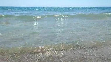 Turkuvaz şeffaf suyla güzel deniz dalgaları güneşli yaz gününde kumlu kumsalda yuvarlanıyor. Sessiz, sakin, rüzgarsız deniz. Düşük açı. Aşağıdan. Hiç kimse. Doğa arkaplanı. Doğal arkaplan