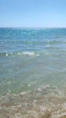 Deniz dalgalarının şeffaf sularından oluşan güzel bir turkuaz. Güneşli bir yaz gününde güneş parlıyor. Deniz kıyısında bir gün. Deniz Burnu. Güneşli bir manzara. Hiç kimse. Doğa arkaplanı Doğal arkaplan Dikey