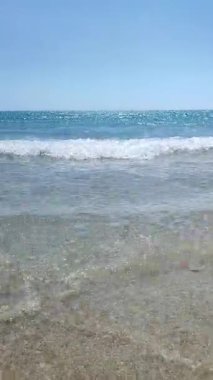 Turkuaz şeffaf suyla deniz dalgaları güneşli yaz gününde kumlu kumsalda yuvarlanıyor. Sakin, rüzgarsız deniz. Düşük açı. Aşağıdan. Hiç kimse. Doğa arkaplanı. Doğal arkaplan dikey