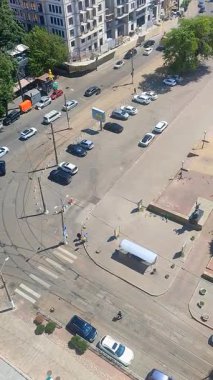 Odessa, Ukrayna, 12 Ağustos 2025, güneşli yaz gününde şehir caddesi. Hareket halindeki arabalar, tramvay rayları, yeşil ağaçlar, binalar, asfalt yolda yürüyen insanlar. Şehir manzarası Üst Görünüm Dikey