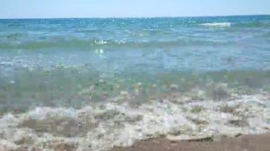 Turkuaz şeffaf suyla deniz dalgaları güneşli yaz gününde kumlu kumsalda yuvarlanıyor. Sessiz, sakin, rüzgarsız deniz. Düşük açı. Aşağıdan. Hiç kimse. Doğa arkaplanı. Doğal arkaplan