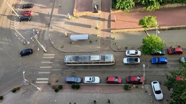 Asfalt yol, hareket halindeki arabalar, tren rayları, park halindeki arabalar, hareket halindeki tramvay ve güneşli bir yaz akşamında yaya geçidinden geçen insanlar. Üst Manzara. Yukarıdan bak. Şehir manzarası