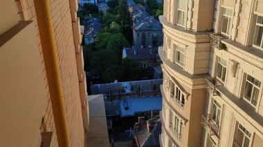 Yaz akşamları şehir manzarası ve güneş ışığı çok katlı bina pencereli beyaz duvarı aydınlatıyor. Eski binalar, çatılar, yeşil ağaçlar. Ön cephede. Mimari