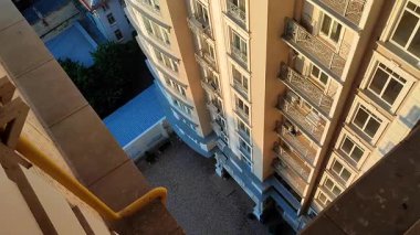 Çok katlı binanın en üst katından bak. Pencereleri ve balkonları asfaltlı kiremitlerin altındaki güneş ve zemin alanı aydınlatan beyaz çok katlı yüksek bina cephesi.