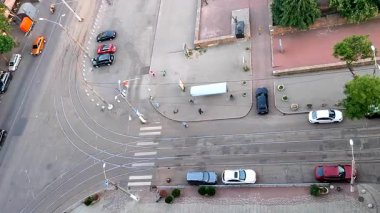 Asfaltlı sokak manzarası, toplu taşıma durağı, ayakta duran insanlar, hareket halindeki arabalar, tramvay rayları, yeşil ağaçlar, yürüyen insanlar ve yaz akşamları park etmiş arabalar. Açık havada. Yukarıdan görüntüle