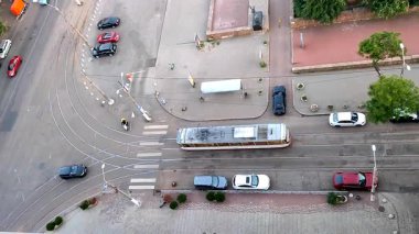 Asfaltlı sokak manzarası, toplu taşıma durakları, duraklar ve hareket halindeki tramvaylar, tramvaylar, tramvaylar, yeşil ağaçlar, yürüyen insanlar ve yaz günü park etmiş arabalar. Açık havada. Yukarıdan görüntüle