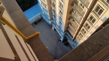 Çok katlı binanın en üst katından bak. Pencereleri ve balkonları asfaltlı kiremitlerin altındaki güneş ve zemin alanı aydınlatan beyaz çok katlı yüksek bina cephesi.