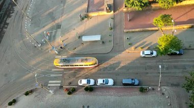 Tramvay kavşağından geçiyor. Yol, tramvay, insanlar, park etmiş arabalar, yaz sabahı yeşil ağaçlar ve gölgeler. Parlayan güneş. Şehir manzarası. Şehir manzarası. Şehir manzarası. Üst Manzara. Yukarıdan Görünüm