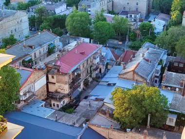 Şehir manzarası. Çatıları olan eski binalar, yeşil ağaçlar, yol ve güneşli yaz akşamlarında hareket eden arabalar. Eski evlerin pencereleri ve duvarları, şehirdeki çok katlı binalar. Şehir manzarası. Şehir manzarası.