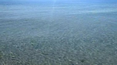 Sığ kumlu deniz kıyısında şeffaf su, güneşli yaz gününde deniz kabukları. Güneş suyun yüzeyinde parlıyor. Deniz kıyısında küçük dalgalar. Doğa arkaplanı. Doğal arka plan. Deniz Burnu.