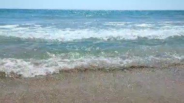 Turkuaz şeffaf suyla deniz dalgaları güneşli yaz gününde kumlu kumsalda yuvarlanıyor. Sessiz, sakin, rüzgarsız deniz. Düşük açı. Aşağıdan. Hiç kimse. Doğa arkaplanı. Doğal arkaplan