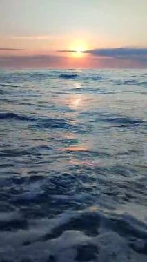 Gün batımında ya da denizde şafakta. Okyanusta gün batımı ya da gün doğumu. Denizin üstünde güneş var. Güneş, gökyüzü, bulutlar, ufuk çizgisi, deniz, deniz dalgaları, kumlu sahil, sahil. Sabah ve akşam sahilde. Dikey