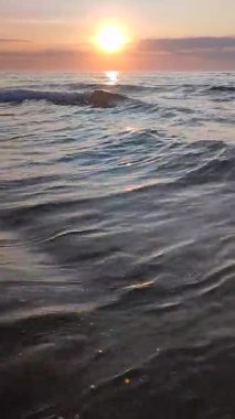 Gün batımında ya da denizde şafakta. Okyanusta gün batımı ya da gün doğumu. Denizin üstünde güneş var. Güneş, gökyüzü, bulutlar, ufuk çizgisi, deniz, deniz dalgaları, kumlu sahil, sahil. Sabah ve akşam sahilde. Dikey