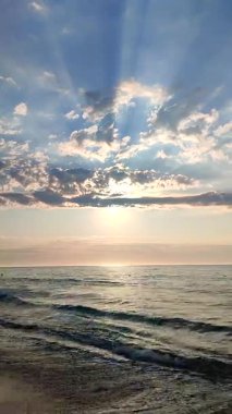 Güzel deniz manzarası. Deniz manzarası. Okyanus manzarası. Sakin denizin mavi suyu, ufuk çizgisi, mavi gökyüzü, beyaz bulutlar, bulutların arasından parlayan güneş ışınları. Güneşli bir sabah. Deniz kıyısında. Doğal arkaplan dikey