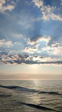 Deniz Burnu. Deniz manzarası. Okyanus manzarası. Sakin denizin mavi suyu, ufuk çizgisi, mavi gökyüzü, beyaz bulutlar, bulutların arasından parlayan güneş ışınları. Güneşli bir sabah. Deniz kıyısında. Doğal arkaplan dikey