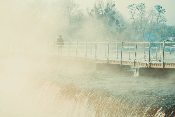 человек, идущий по мосту через реку зимой
