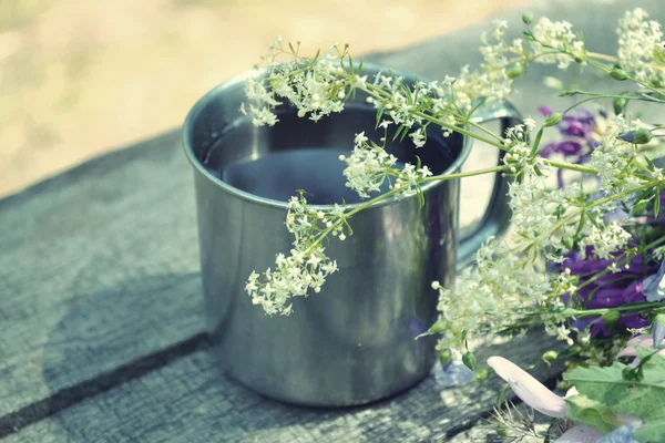 Cup of tea standing on a table with blooming flowers — Stock Photo, Image