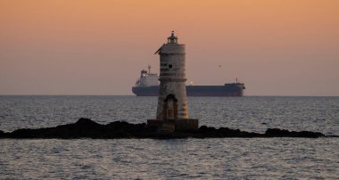 Arkasında kargo gemisi olan Calasetta al traomonto deniz feneri.