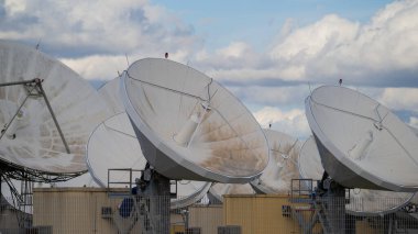 Bulutları ve endüstriyel yapıları olan bir telekomünikasyon tesisinde uydu anteni.