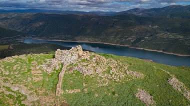 Sardunya 'nın dramatik gökyüzü altında yeşil manzaradan yükselen tarih öncesi nuraghe taşı yapısı