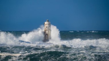Güçlü fırtına dalgaları, ıssız bir deniz fenerine çarpıyor. Açık deniz koşullarında duruyor..