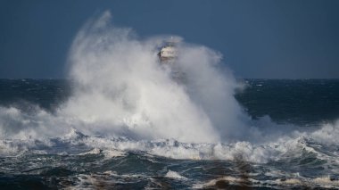 Güçlü fırtına dalgaları, ıssız bir deniz fenerine çarpıyor. Açık deniz koşullarında duruyor..