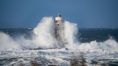 Güçlü fırtına dalgaları, ıssız bir deniz fenerine çarpıyor. Açık deniz koşullarında duruyor..