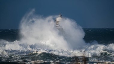 Güçlü fırtına dalgaları, ıssız bir deniz fenerine çarpıyor. Açık deniz koşullarında duruyor..