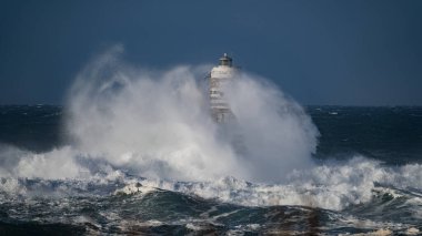 Güçlü fırtına dalgaları, ıssız bir deniz fenerine çarpıyor. Açık deniz koşullarında duruyor..