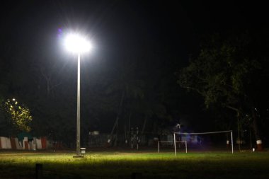 Halojen lamba geceleri boş spor sahasında direğin üzerinde parlıyor.
