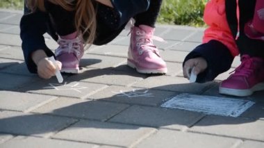 Küçük kız elleri kaldırım kenarında beyaz tebeşirle çiziyor.