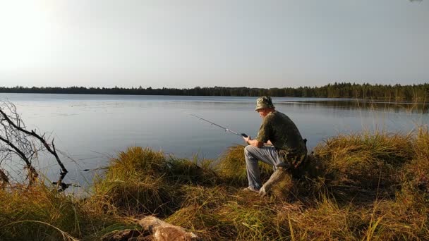 Um pescador na natureza está pescando com uma vara no lago e lendo as notícias — Vídeo de Stock