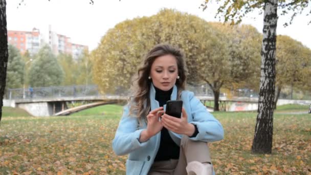 Elegante ragazza in un parco autunnale si siede sull'erba — Video Stock