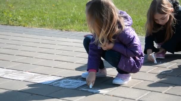İki küçük kız kaldırıma pastel boyayla resim çiziyor. — Stok video