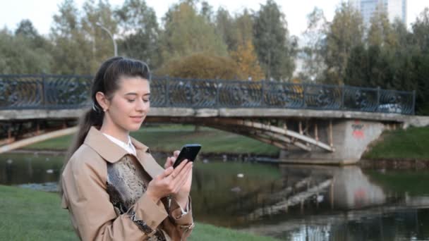 Bella ragazza in un parco cittadino scrive un messaggio sul suo telefono — Video Stock