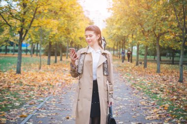 Güz parkında elinde cep telefonuyla güzel bir kız.