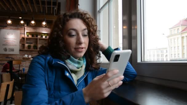 Girl sitting in a fast food restaurant and writing a message on smartphone — Stock Video